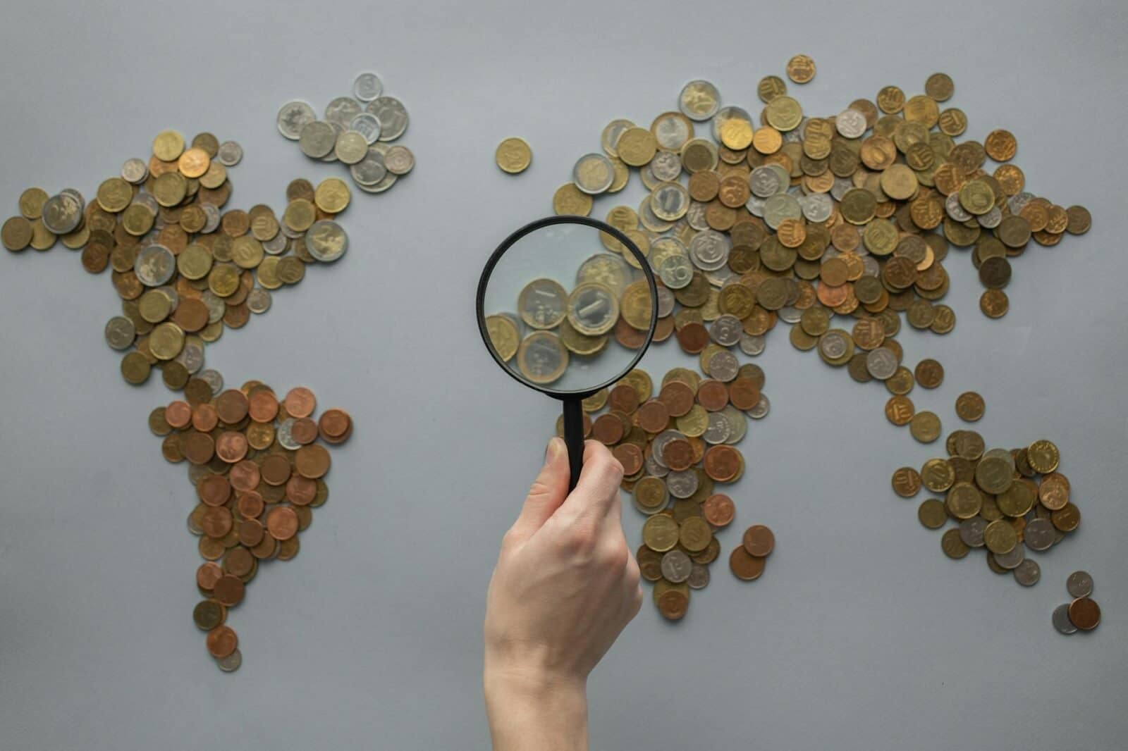 anonymous person with magnifying glass over world map of coins