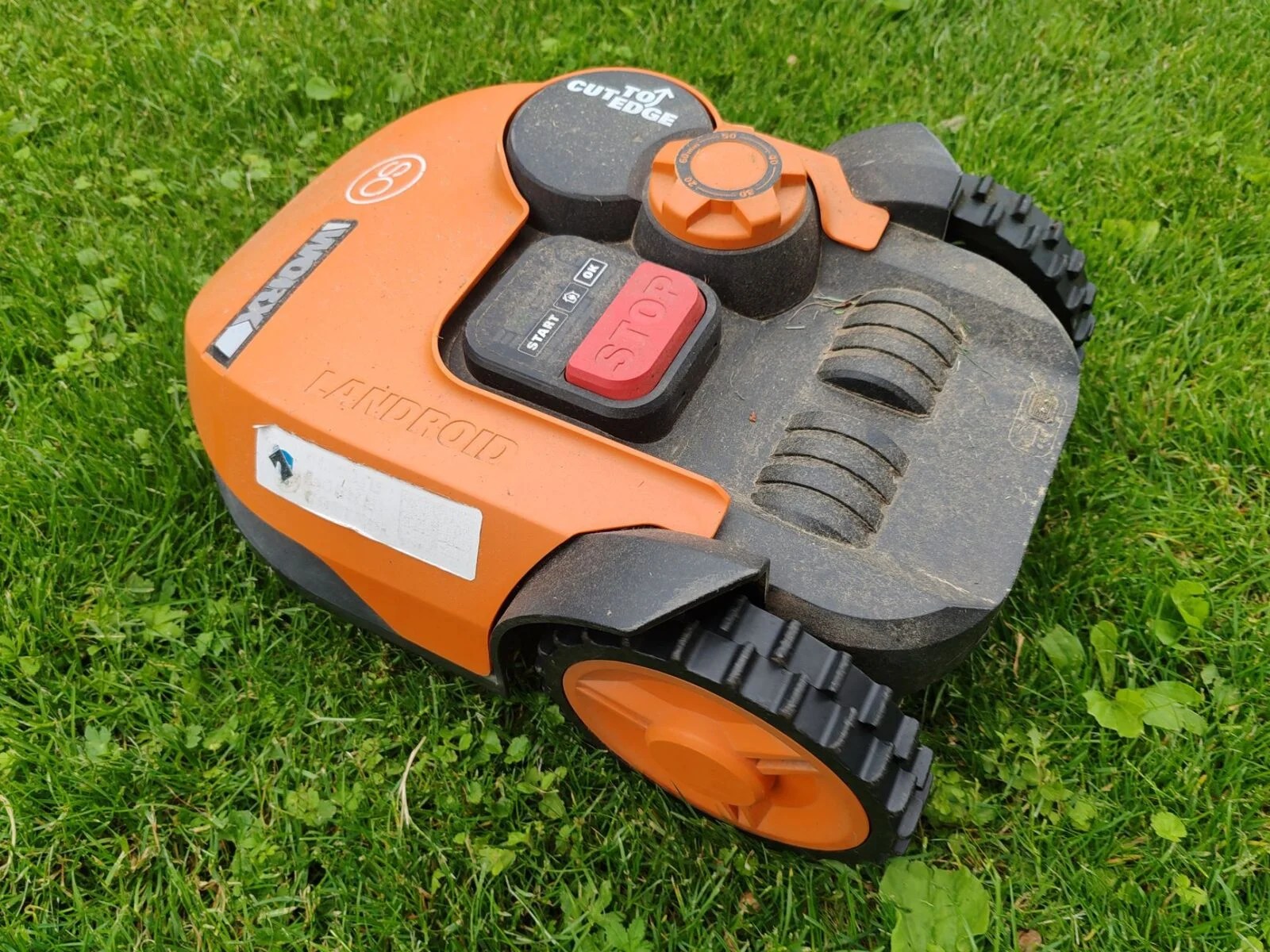 orange robotic lawn mower on fresh green grass